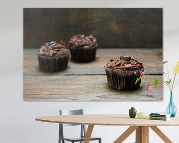 three chocolate cupcakes with cocoa butter cream on dark wood, one is in focus, copy space, narrow d by Maren Winter