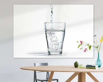 water wordt in een drinkglas gegoten, geïsoleerd op een witte achtergrond met kopieerruimte van Maren Winter