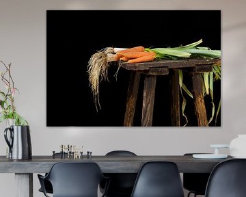 organic carrots and leeks harvested from the vegetable garden on an old wooden stool against a black by Maren Winter