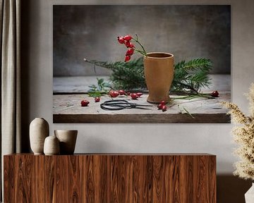 het voorbereiden van natuurlijke kerstversiering met rozenbottels in een aardewerken vaas en dennent van Maren Winter