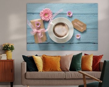 Kaffeetasse, rosa Blumen und ein Geschenk auf pastellblauem Holzgrund mit Kopierfeld, Text Guten Mor von Maren Winter