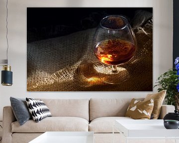 Cognac or brandy in a glass with a glowing light reflex on rustic burlap, concept for enjoyment or a by Maren Winter