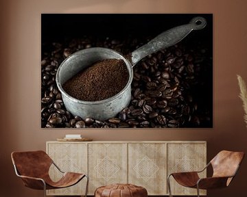 small metal pot with ground coffee on a heap of whole roasted coffee beans, dark background, closeup by Maren Winter