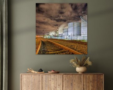 Oil refinery at night with rails and silos against a cloudy sky by Tony Vingerhoets