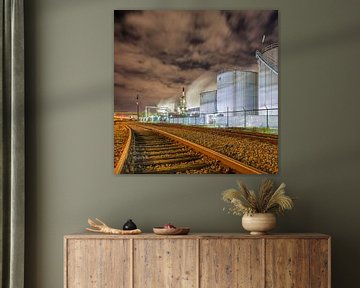 Oil refinery at night with rails and silos against a cloudy sky