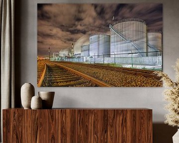 Oil refinery at night with rails and silos against a cloudy sky by Tony Vingerhoets