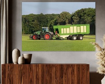 Groene tractor die gemaaid gras opraapt met een groene opraapwagen in de zomer in Nederland van Tonko Oosterink