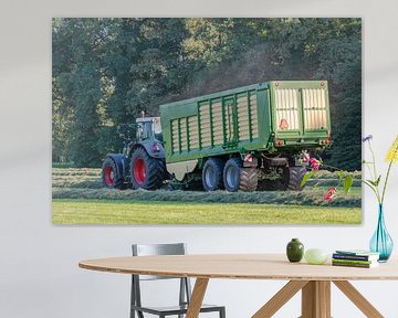 Groene tractor die gemaaid gras opraapt met een groene opraapwagen in de zomer in Nederland