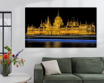 Hungarian parliament building at night with boat passing by by Hannon Queiroz