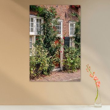 Vorderes Backsteinhaus mit Holztür und Rosenbusch und Stockrosen