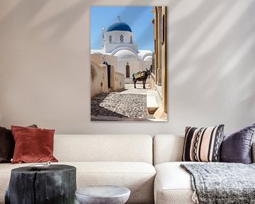 Straße in einem Dorf auf der griechischen Insel Santorin, mit weiß-blauer Kirche und Esel.