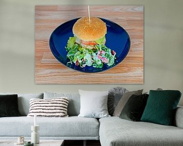 Cheeseburger mit Feldsalatgarnitur auf blauem Teller serviert