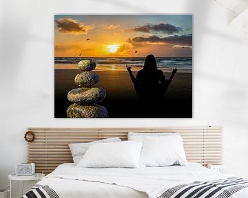Balancesteine am Strand mit Sonnenuntergang und einer Frau die Meditiert von Animaflora PicsStock