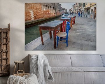 Tafeltjes met stoelen aan kanaal met boten in oude centrum Venetie, Italie van Joost Adriaanse