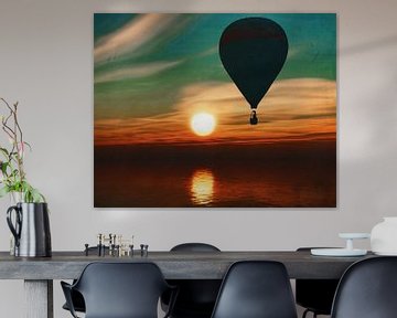 A hot air balloon travels over the sea during sunset