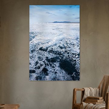 Dünner Schnee bildet skurrile Muster auf dem Eis des Baikal und Berge in der Ferne mit dem Himmel