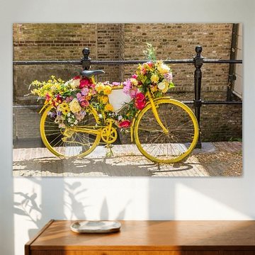 Een oude gele fiets versierd met bloemen staat tegen het hek van een gracht in Gouda