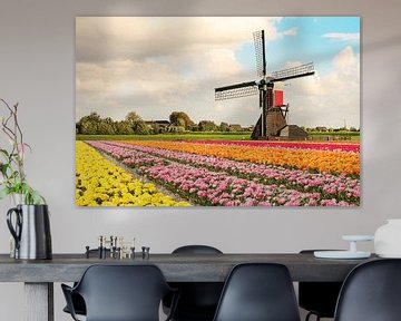 Een veld met bloeiende tulpen met op de achtergrond een molen en Hollandse wolken lucht van Henk van den Brink