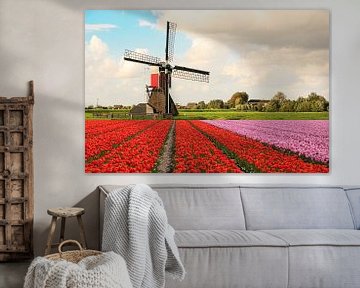 Een veld met bloeiende tulpen met op de achtergrond een molen en Hollandse wolken lucht van Henk van den Brink