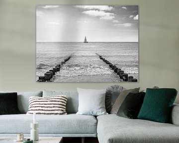Sailing boat between beach posts in Zeeland, black and white by Evelien Oerlemans