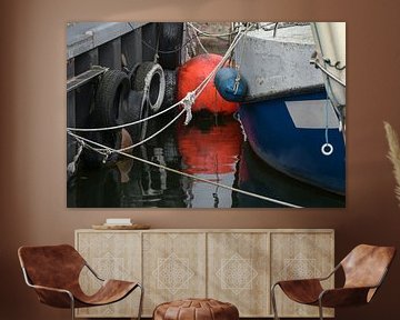 Orange buoy with reflection in the water and detail of a fishing boat tied at the dock in the port,  by Maren Winter