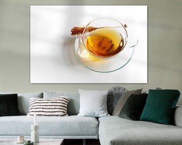 Glass cup half full with black tea and a stick of rock candy with reflecting shadow on a white backg by Maren Winter
