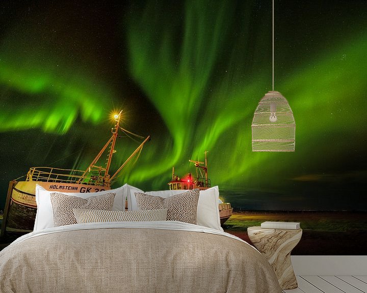 Sfeerimpressie behang: Noorderlicht in de nacht op IJsland met een schitterend lichtspel in de lucht en een oud vissersschi van Bas Meelker