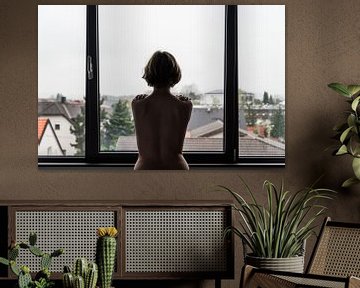 Young white woman standing in front of a window, facing her back