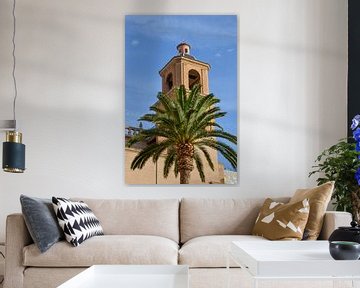 Een toren van de Basiliek van de Heilige Maria van Alicante achter groene palmbomen onder een strakb van LuCreator