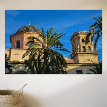 Die Kuppel und ein Turm der Basilika der Heiligen Maria von Alicante hinter grünen Palmen unter blau